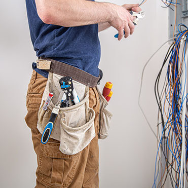 electrician-builder-at-work-examines-the-cable-connection-in-the-electrical-line-in-the-fuselage-of-an-industrial-switchboard-professional-in-overalls-with-an-electrician-s-tool